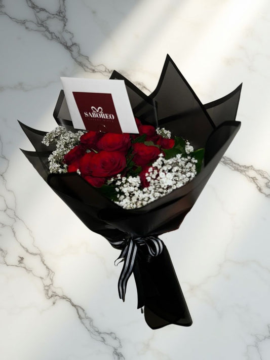Bouquet of red roses with black wrap and white card on a marble surface