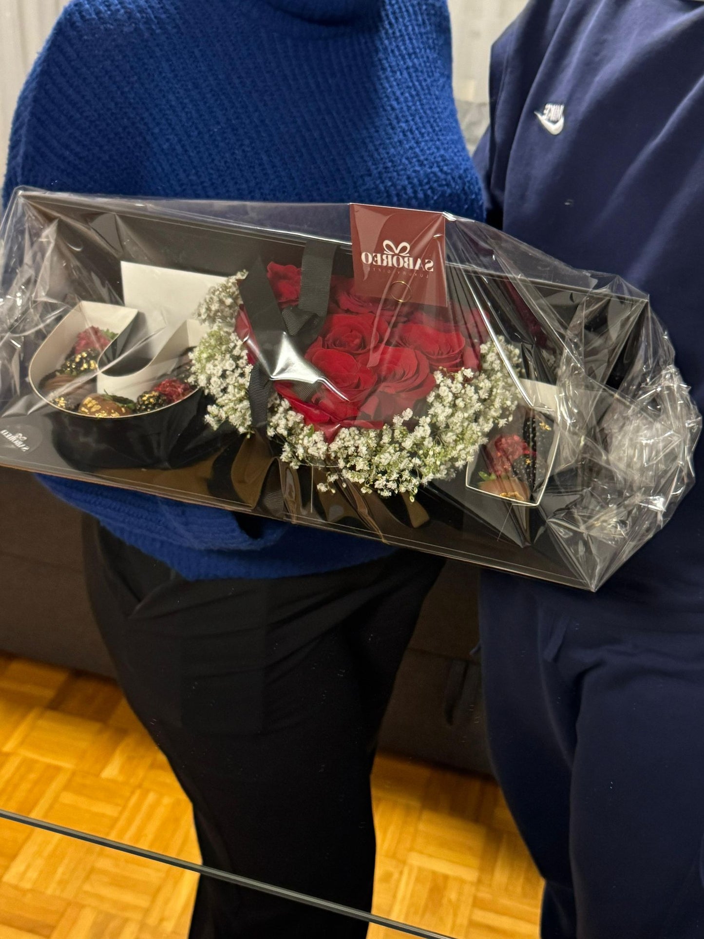 Person holding a bouquet of flowers wrapped in clear plastic luxury chocolate-covered strawberries with gold leaf Zürich