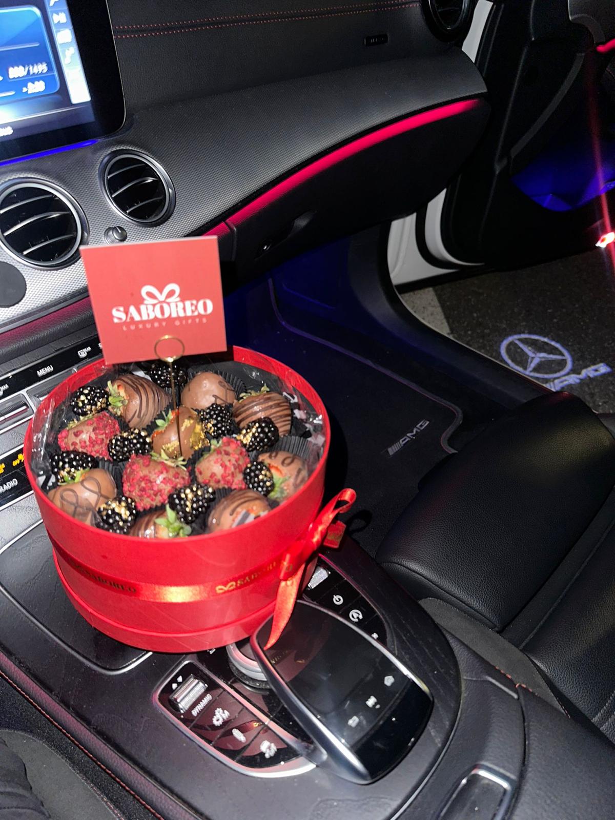 Red gift box with chocolates on a car's center console, featuring the brand 'Sarobeo'. luxury chocolate-covered strawberries with gold leaf Zürich