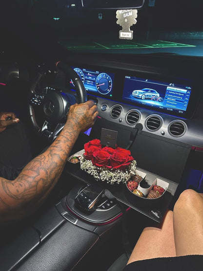 Person sitting inside a car with a flower arrangement on the dashboard luxury chocolate-covered strawberries with gold leaf Zürich, red roses